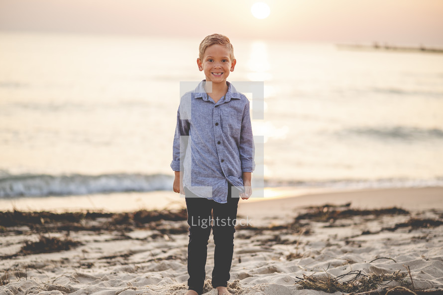 young boy standing on a beach at sunset 