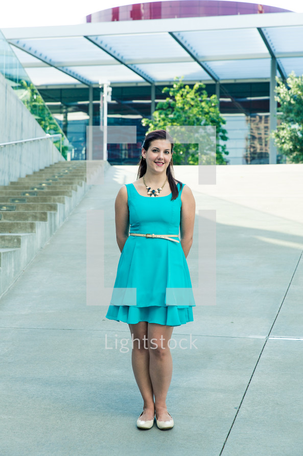 a woman in a blue dress standing outdoors in front of steps 