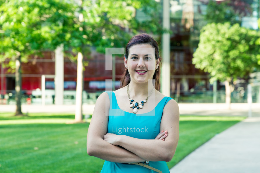 a portrait of a young woman standing in front of a campus in a blue dress 