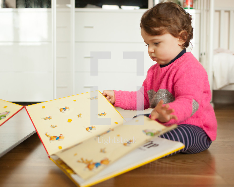 Toddler baby girl playing with fairy tales book on the oak wood floor.