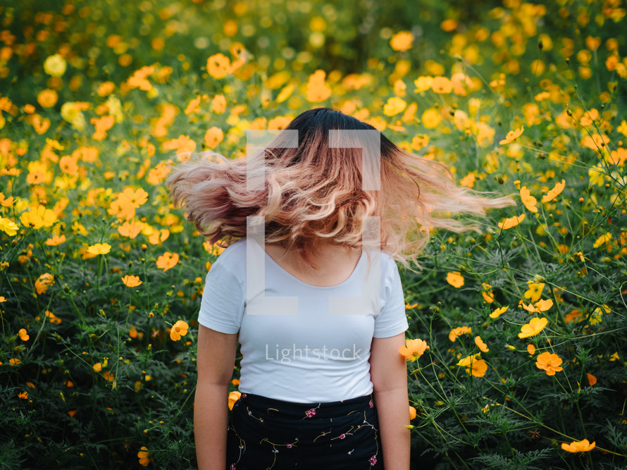 a woman flipping her hair in a field of yellow flowers 