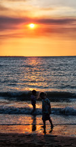 kids playing in the ocean on a beach at sunset 
