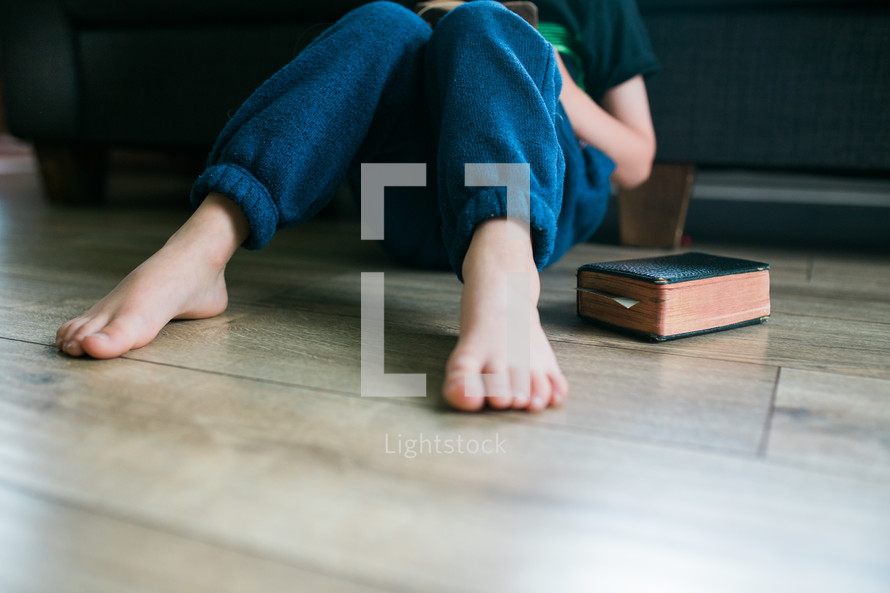 a boy sitting on the floor reading a Bible 