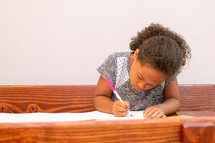 a little girl drawing at a table 