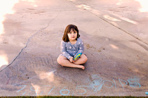 a child sitting on concrete next to chalk drawings 