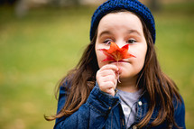 a little girl holding a fall leaf in front of her face 