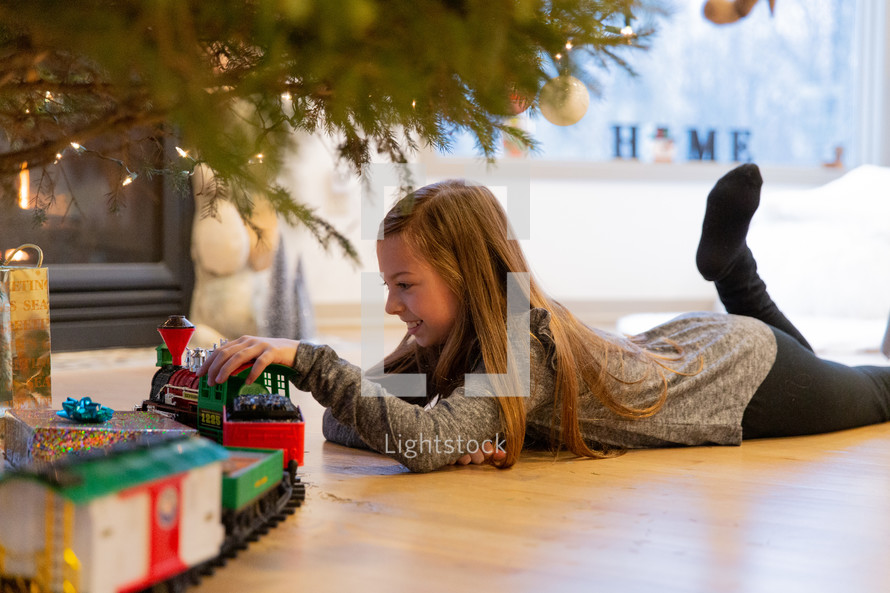 little girl playing with a train under a Christmas tree