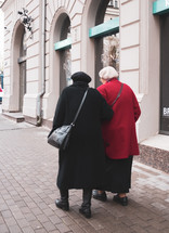 elderly women friends walking down a sidewalk 