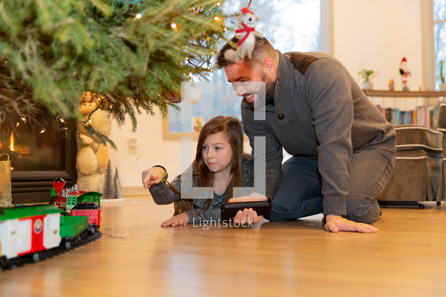 father and daughter playing with a toy train under a Christmas tree
