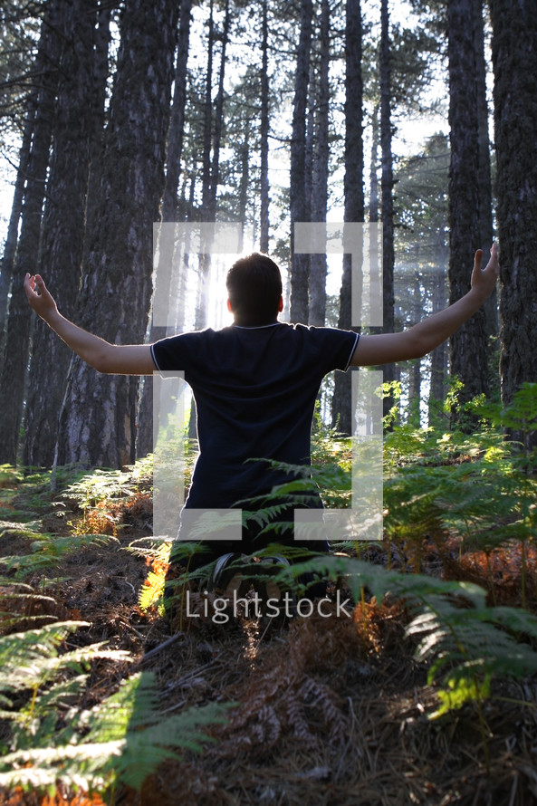 man standing in a forest with his hands raised in worship to God