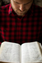 a man in a plaid shirt reading a Bible 