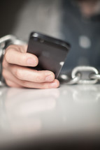 Wrists bound with chain holding a cell phone.