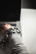 man bound in chains and on a laptop 
