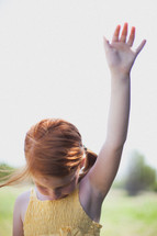 Girl standing outside with arm raised.