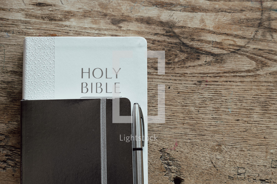 Bible, notebook, and pen on a wooden table