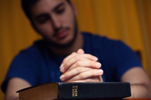 a man with praying hands over a Bible 