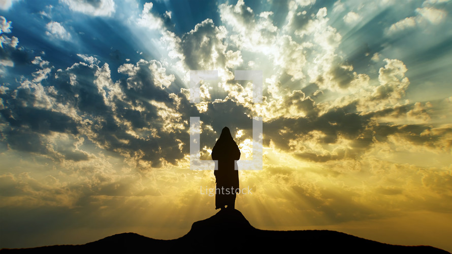 Silhouette of Jesus standing on a mount with sun rays and mystic clouds.

