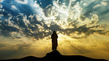 Silhouette of Jesus standing on a mount with sun rays and mystic clouds.
