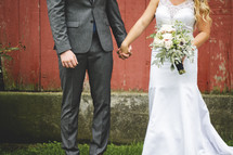 portrait of a bride and groom against a red barn 