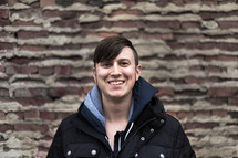 Smiling man wearing a winter coat sanding in front of a brick wall.