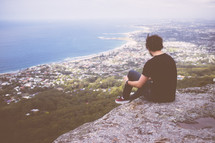 A man sitting at the edge of cliff looking out 