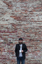 Bearded man with a cup of coffee standing in front of a brick wall.