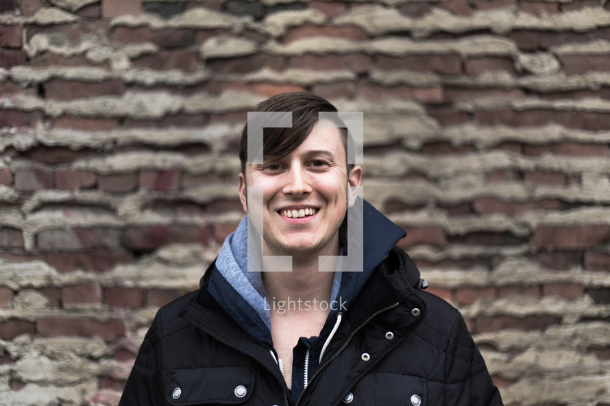 Smiling man wearing a winter coat sanding in front of a brick wall.