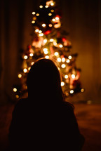 a little girl looking at a Christmas tree 