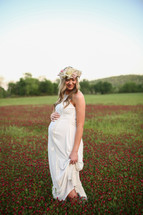 a pregnant woman in a white dress standing in a field of wildflowers 