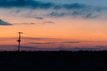 colors of dusk glow behind a powerline and grass