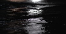 Rain puddles and falling drops against car city lights