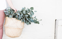 a woman holding a basket with eucalyptus 