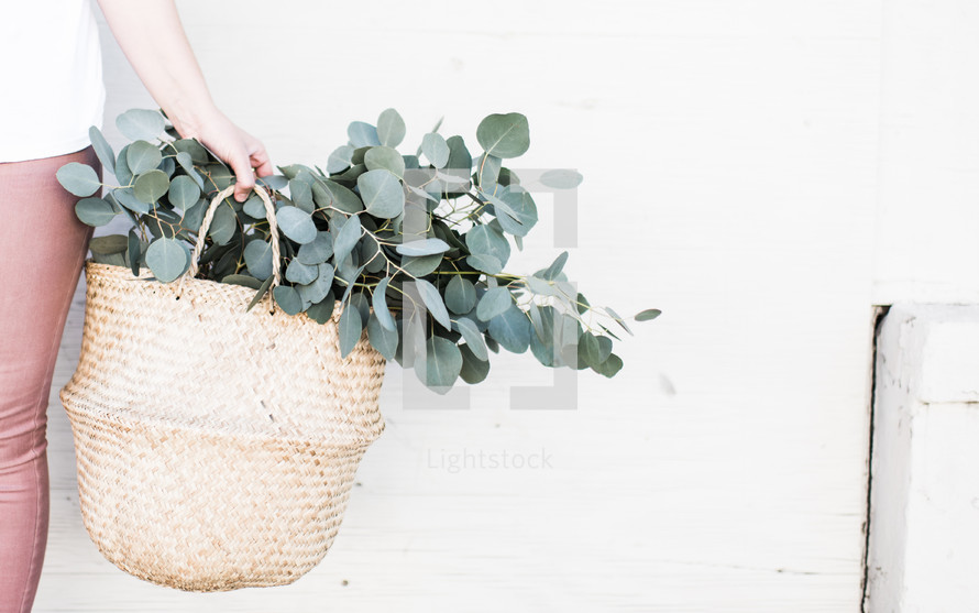 a woman holding a basket with eucalyptus 