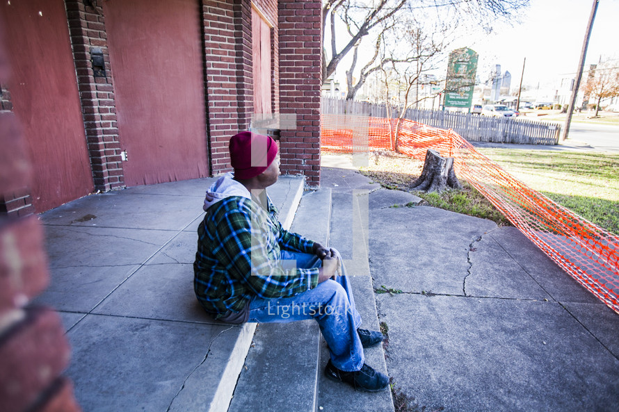 homeless man sitting on stairs in front of a condemned building