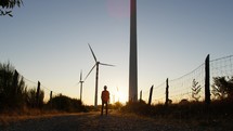 Silhouette of Engineer walking against wind power plant generator at sunset