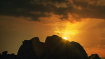 Silhouette of the Cross on mountain at sunset with rays
