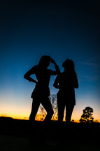 silhouettes of girls standing outdoors at dusk 