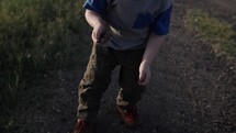 A young happy boy playing, throwing dirt and rocks outside in the sunset or sunrise sunlight on a summer evening in Kansas in cinematic slow motion.