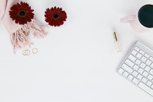 computer keyboard, nail polish, coffee mug, red gerber daisies, gold rings, white background 