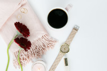 candle, pink scarf, red gerber daisies, watch, nail polish, coffee mug, gold rings, white background 