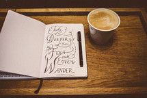 Journal with a pen, and a cup of coffee on a wooden desk.