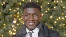 smiling young man standing in front of a Christmas tree 