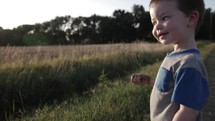 A young happy boy playing, throwing dirt and rocks outside in the sunset or sunrise sunlight on a summer evening in Kansas in cinematic slow motion.