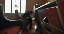 Young, emotional, anxious, and stressed man with long hair and black suit sitting in old church in worship and praying.