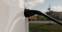 Electric car charging outdoors in summer - close up on plug sticking in car