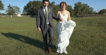 Happy newly married couple, bride and groom walking together outside after summer wedding.