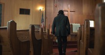 Man in black suit walking in slow motion into church building with cross and pulpit.