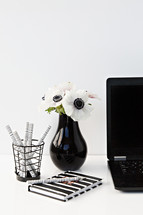  pens in a jar, journal, flowers in a vase, and laptop computer on a desk