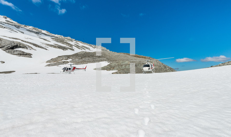 Helicopters landing on a snow covered mountaintop.