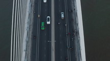 Top down aerial shot of traffic on the bridge over the river in the city, cars and motorbikes riding on asphalt road
